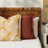 maison venu teracotta pillow propped up on a bed with floral pillow and nightstand with bud vase filled with flowers