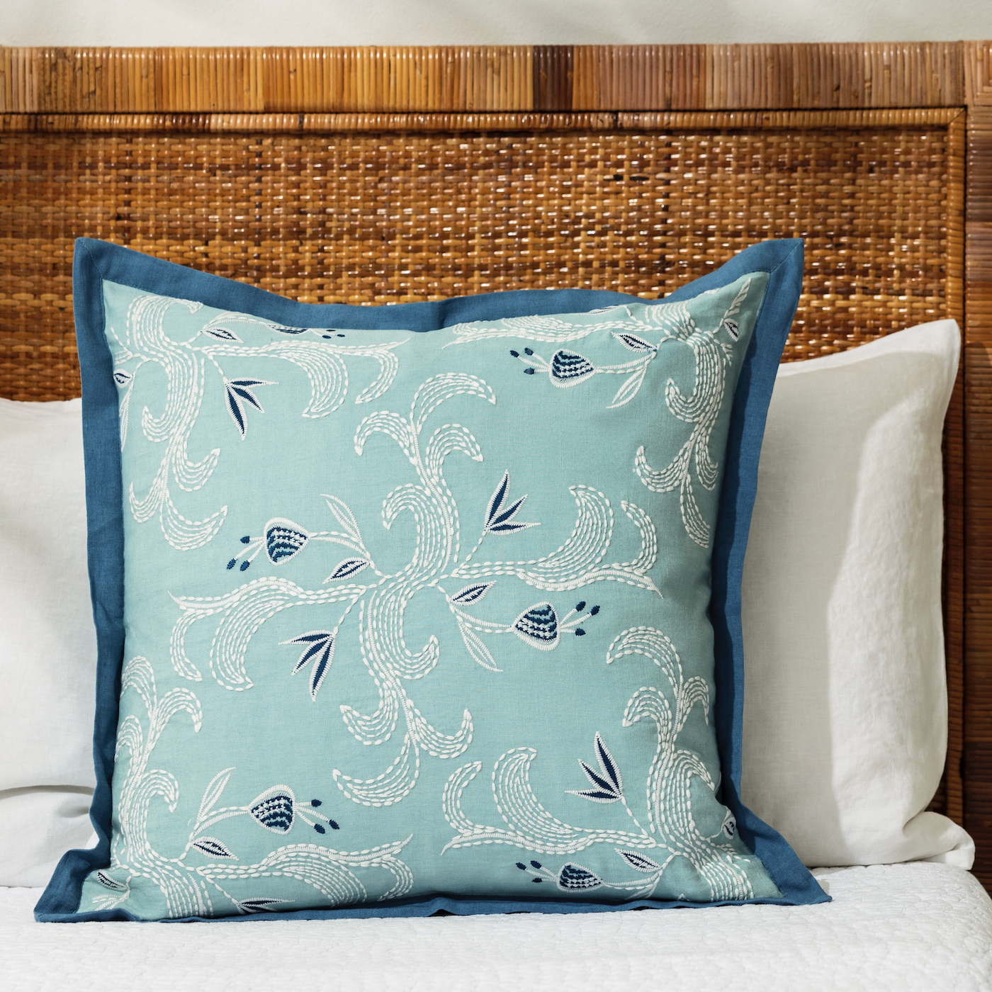 marseille cobalt pillow styled on a bed with white linens against a can headboard