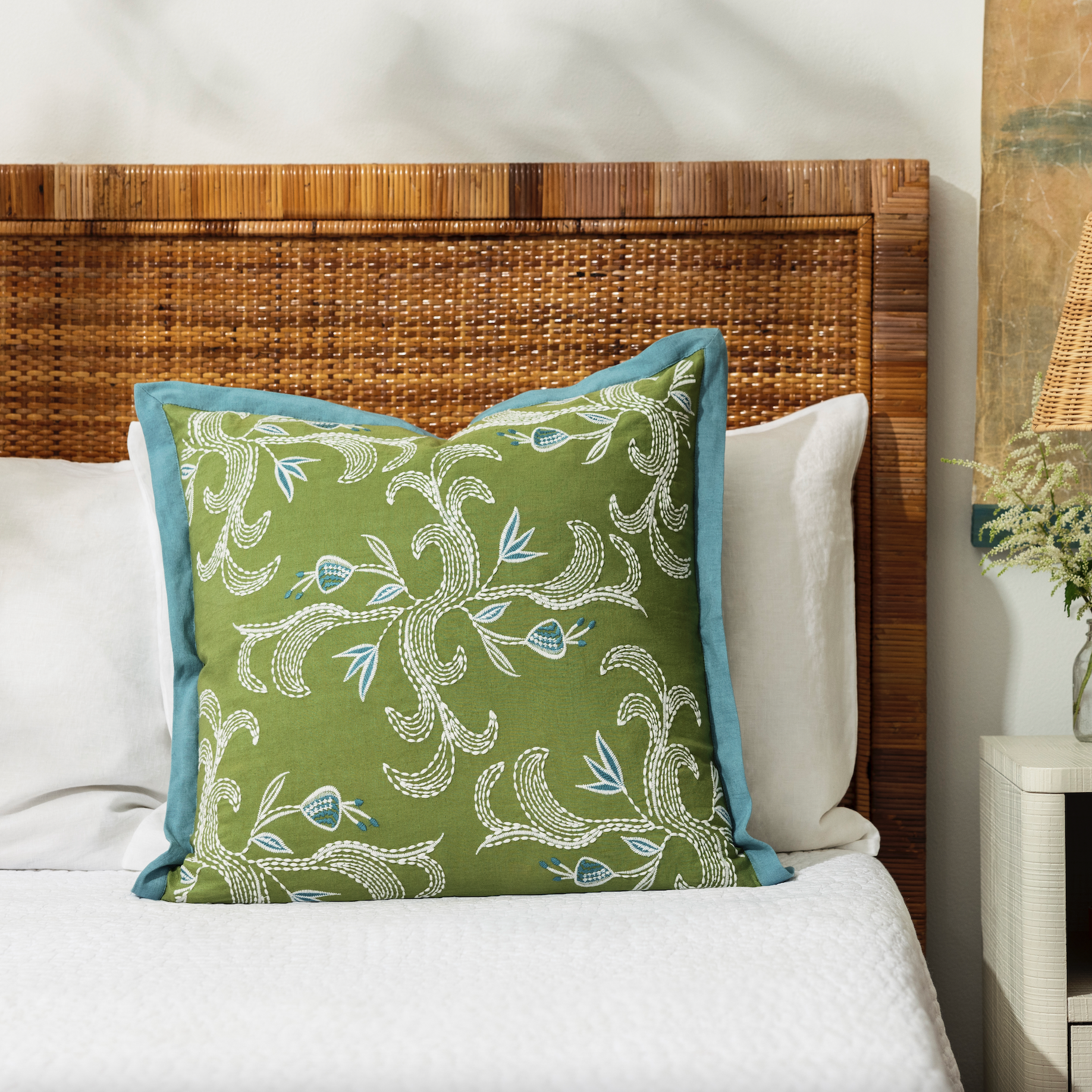 marseille verdant pillow placed on a bed with white bed linen and cane bedhead