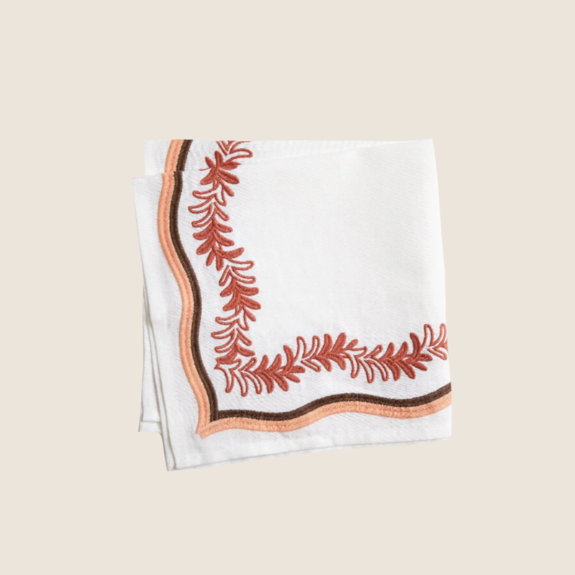 terracotta and gold embroided pattern on a white napkin