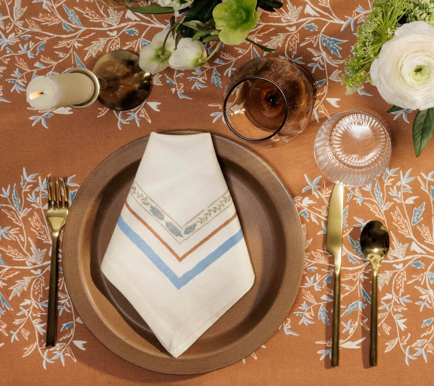 Holly Vine napkin placed on a brown charger placer setting with a taper candle and hellebore and ranunculus flowers