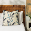 tuileries lapis pillow styled on a bed with white bed linen next to a nightstand with a bud vase containing astilbe flower