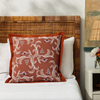 marseille persimmon pillow styled on a bed with white bed linen and a nightstand with flowers in a bud vases and nightstand lamp