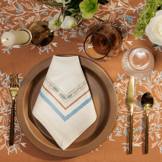 Holly Vine napkin placed on a brown charger placer setting with a taper candle and hellebore and ranunculus flowers