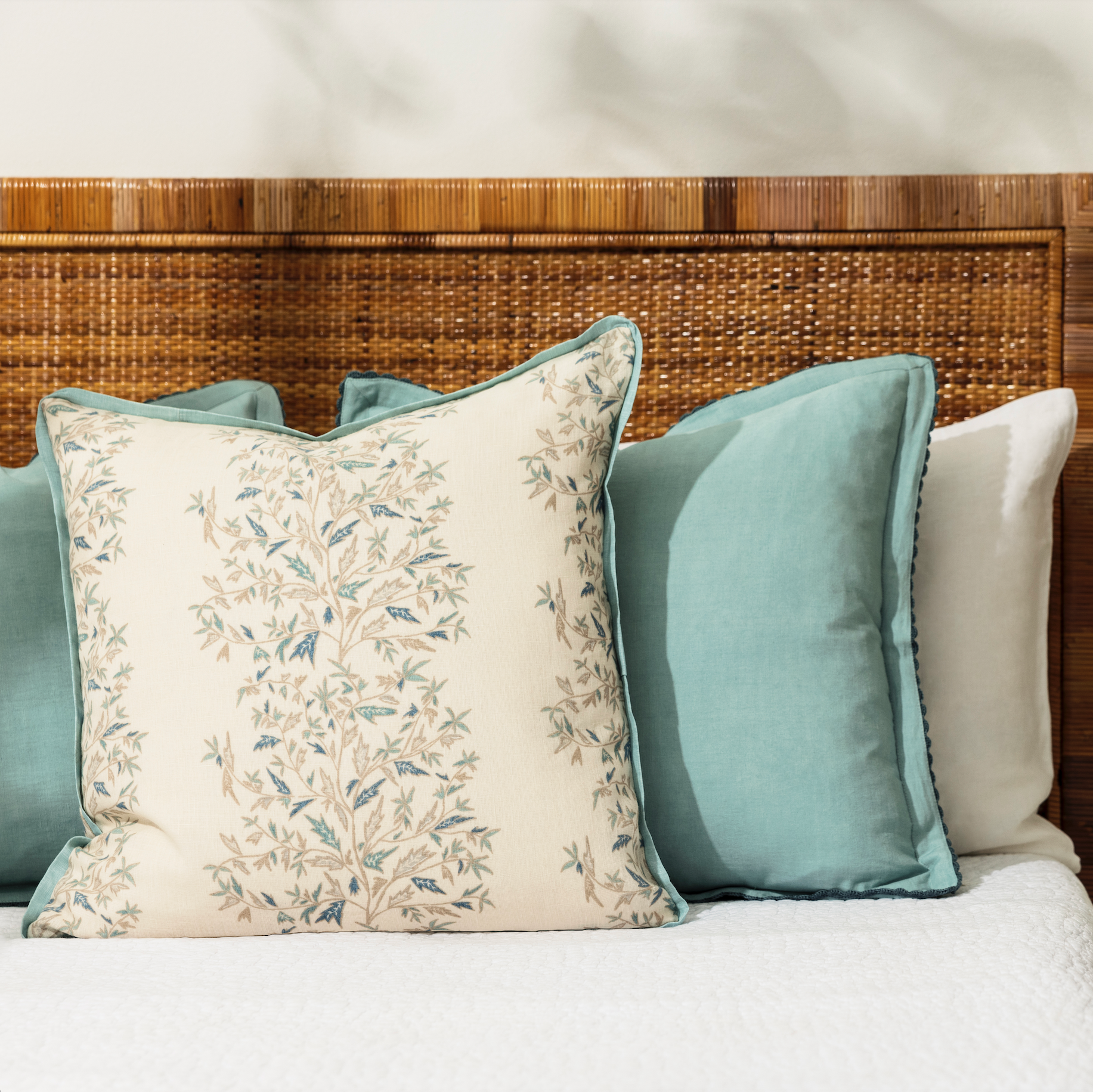 holly vine mer pillow styled on a bed with white bedlinen and cane bednead